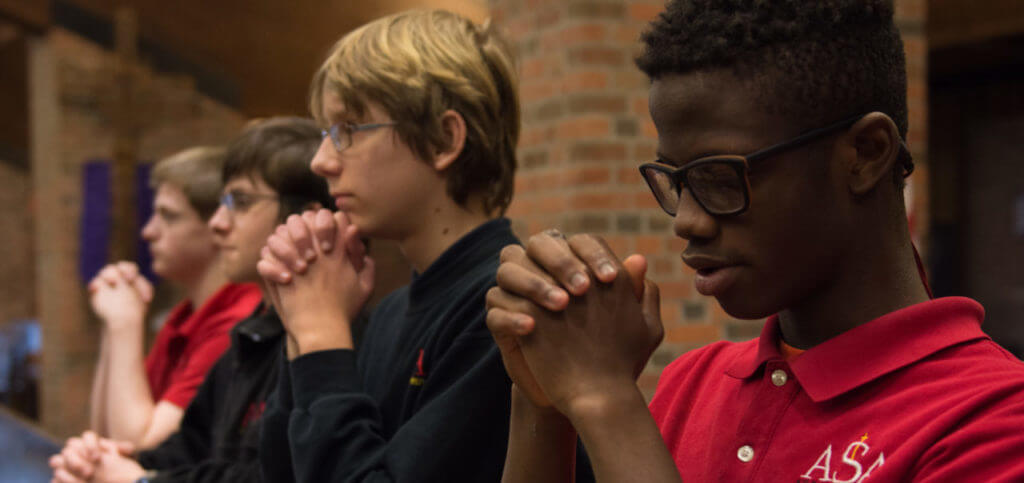 four middle school boys praying in a pew at st. jude catholic church in grand rapids, michigan