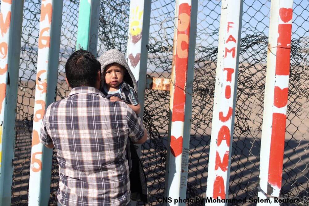 CNS image of a man looking across the border holding his child by Mohammed Salem, Reuters