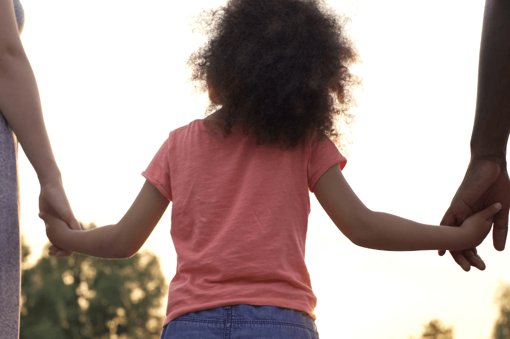 Image of child holding the hands of her parents