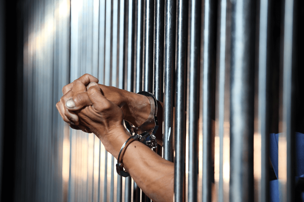 Man wearing hand cuffs clasps hands through cell bars