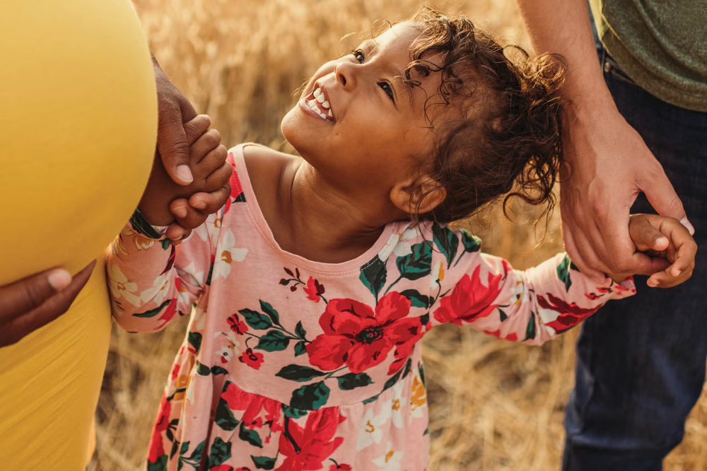 An African American girl smiles up at her pregnant mother's belly