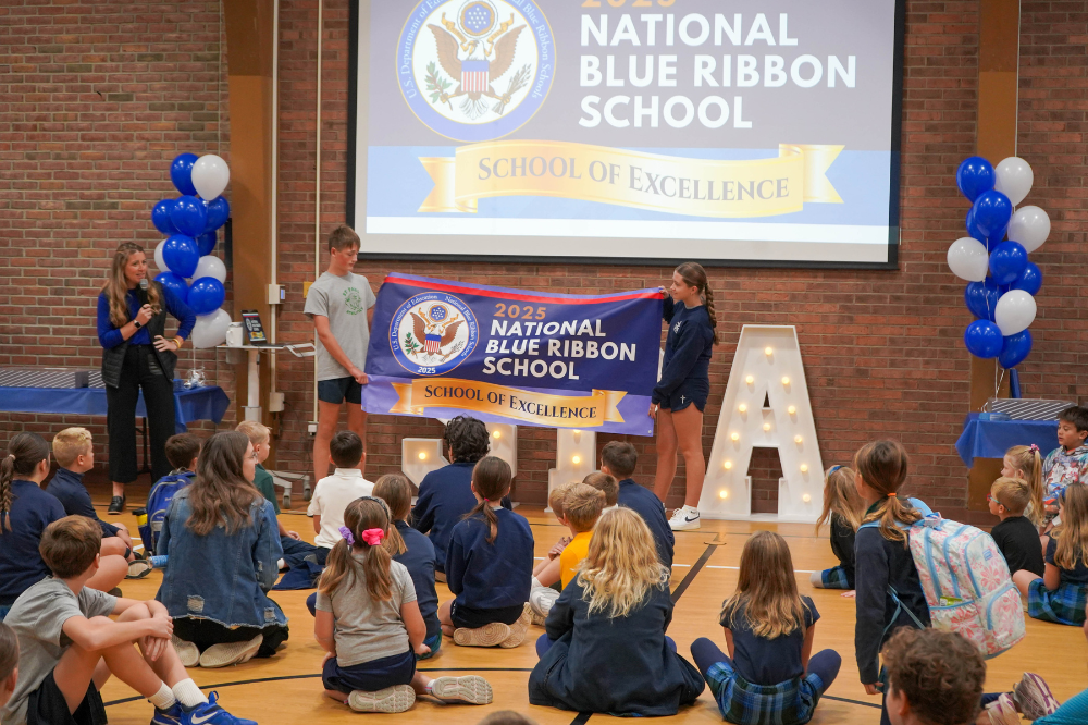 Principal Michelle Morrow of St. Paul the Apostle Catholic School stands in front of school children while the school's 2025 National Blue Ribbon banner is unveiled.