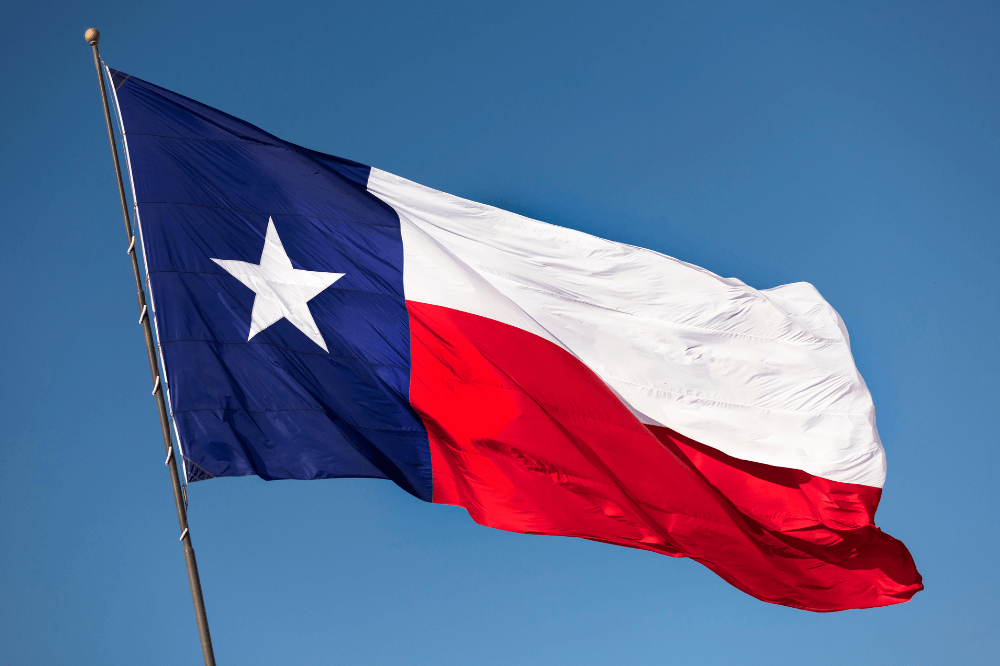 State of Texas flag flying on a flagpole on a clear blue sky day